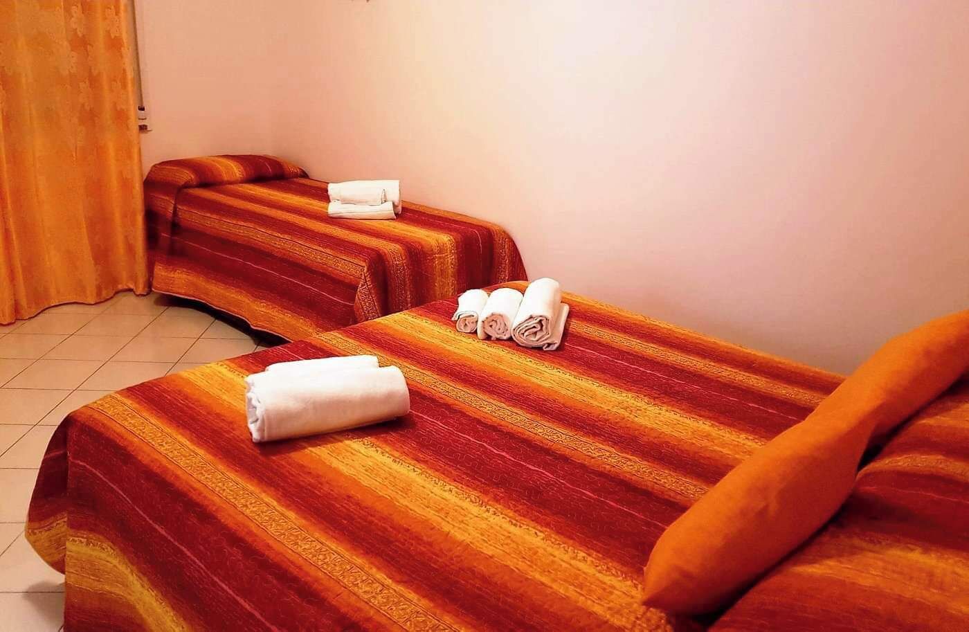 Quarto de hotel com duas camas, cada uma com um cobertor listrado e uma toalha enrolada.