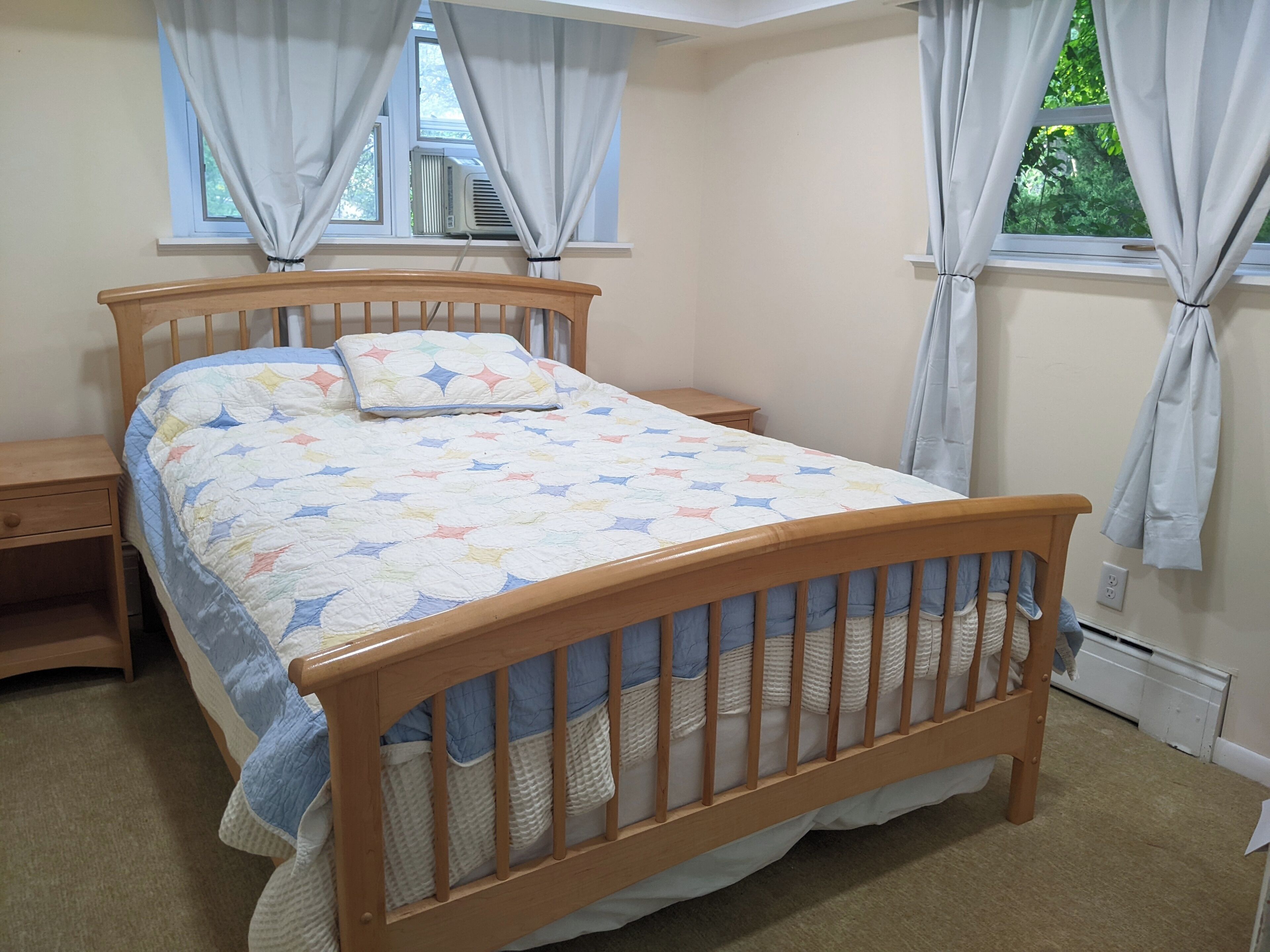 Un dormitorio con una cama de madera, una mesita de noche, una ventana con cortinas y un radiador.