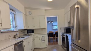 A modern kitchen with white cabinets, stainless steel appliances, and a dining area with wooden chairs and a chandelier. - UM Football - 5 blocks to Stadium (Ann Arbor)
