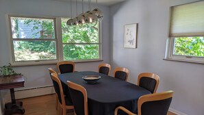 A dining area with a table and chairs, large windows with a view of greenery, and a hanging light fixture. - UM Football - 5 blocks to Stadium (Ann Arbor)