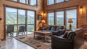 Una habitación amplia con un techo de madera grande, varias ventanas con vista a la montaña, un sofá de cuero y una mesa de centro de madera.