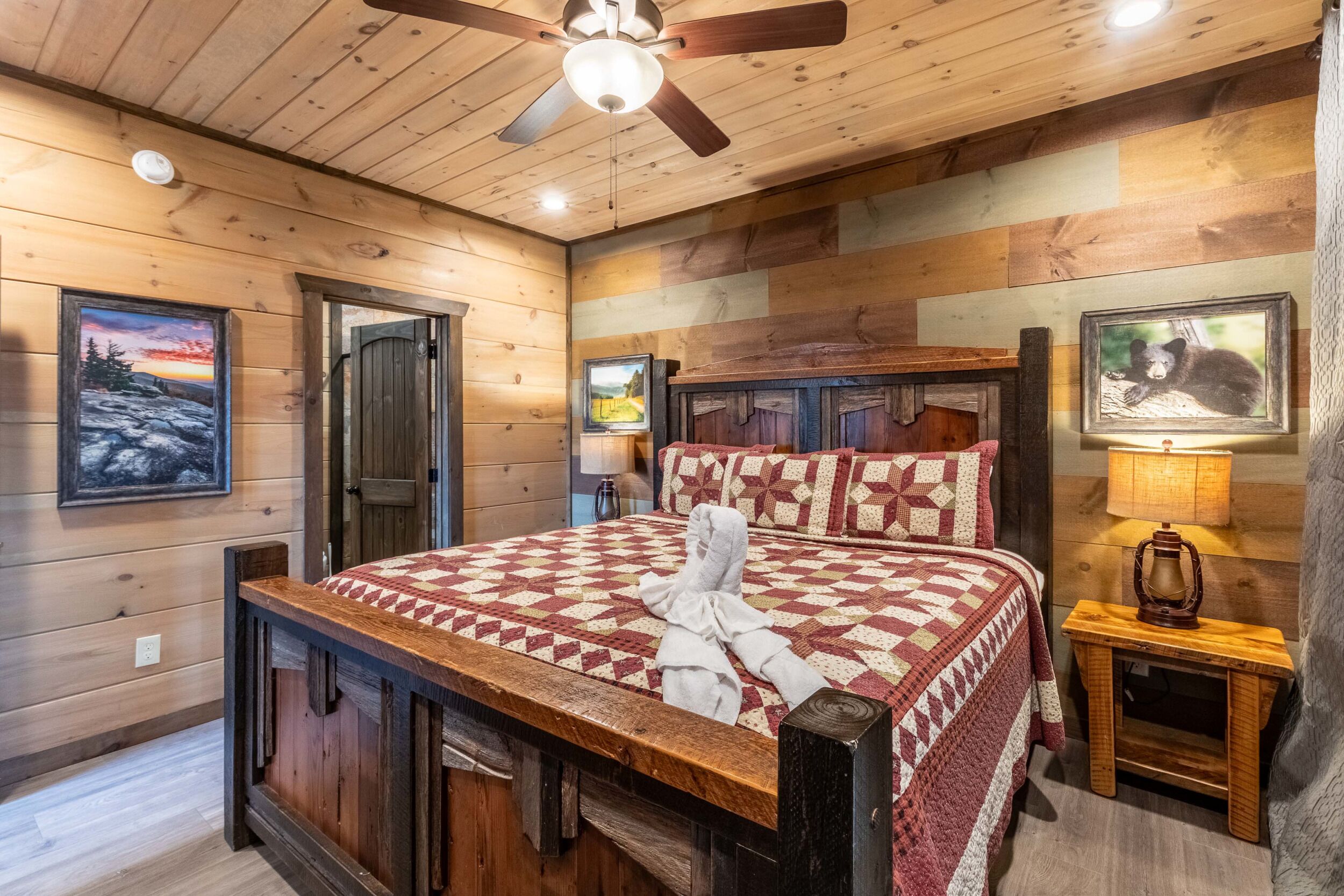 A wooden cabin-style bedroom with a large bed, wooden headboard, and a ceiling fan.