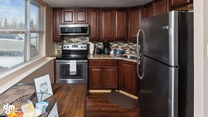 A kitchen with wooden cabinets, a stainless steel refrigerator, a microwave, an oven, and a coffee maker. - Last frontier Rental Family #1 (Anchorage)