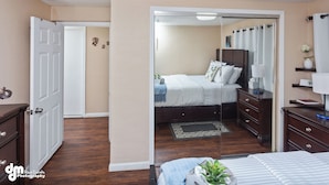 A bedroom with a bed, bedside tables, a dresser, a mirror, a door, and a small plant. - Last frontier Rental Family #1 (Anchorage)