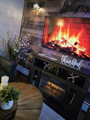 A fireplace with a TV above it, a sign that says 'thankful,' and a plant on the side. - Last frontier Rental Family #1 (Anchorage)