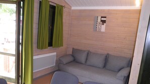 Une pièce chaleureuse avec un canapé gris, deux fauteuils et une fenêtre ornée de rideaux verts.
