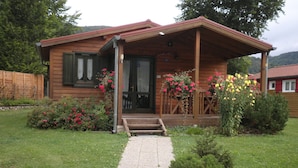 Une cabane en bois dotée d’un porche, d’un chemin de gravier menant à l’entrée et de jardinières ornées de fleurs rouges et jaunes.