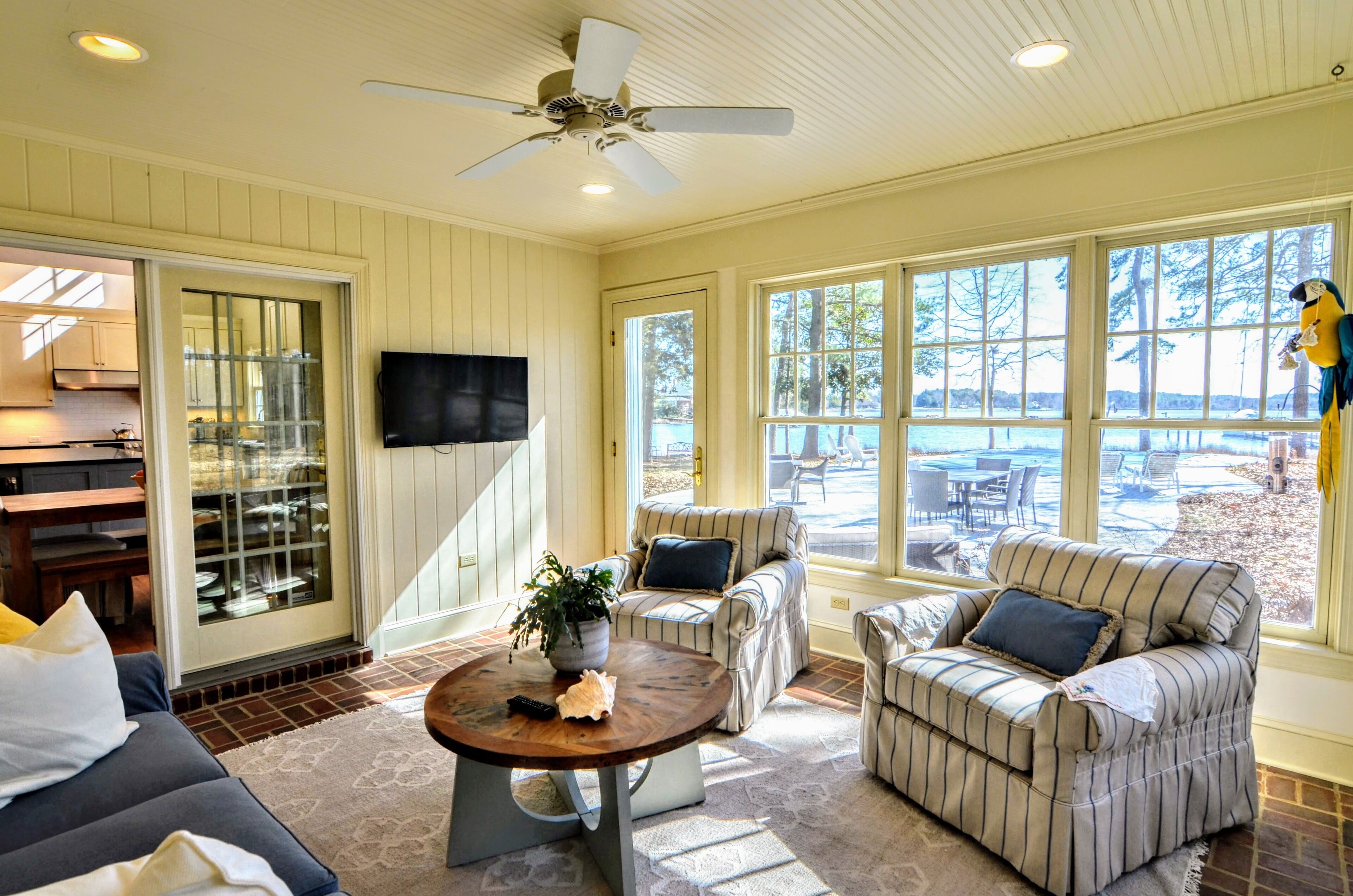 A sunlit room with a ceiling fan, a television, and large windows offering a view of the outdoors.