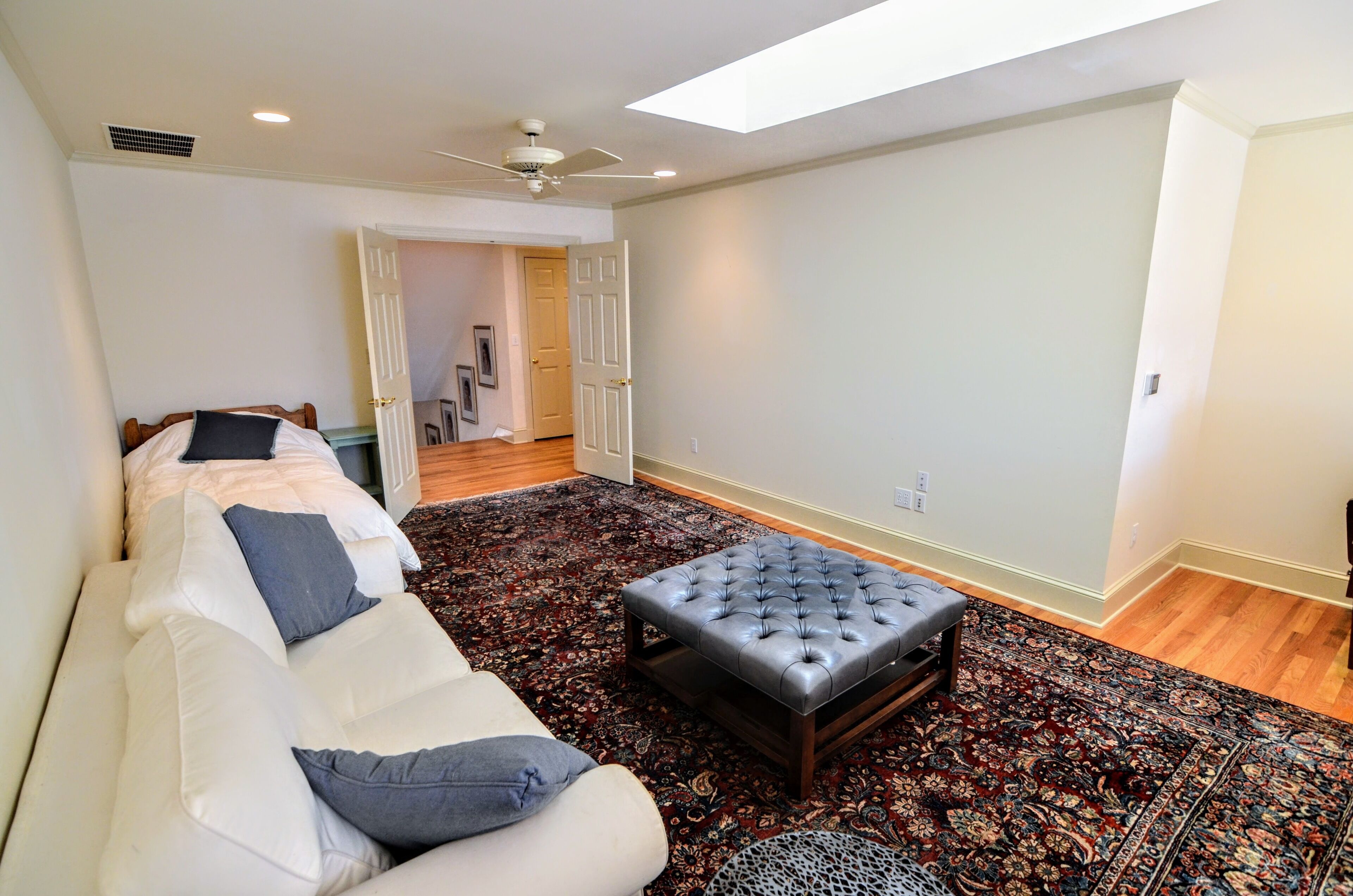 A spacious living room with a large sofa, a tufted ottoman, and a patterned rug.