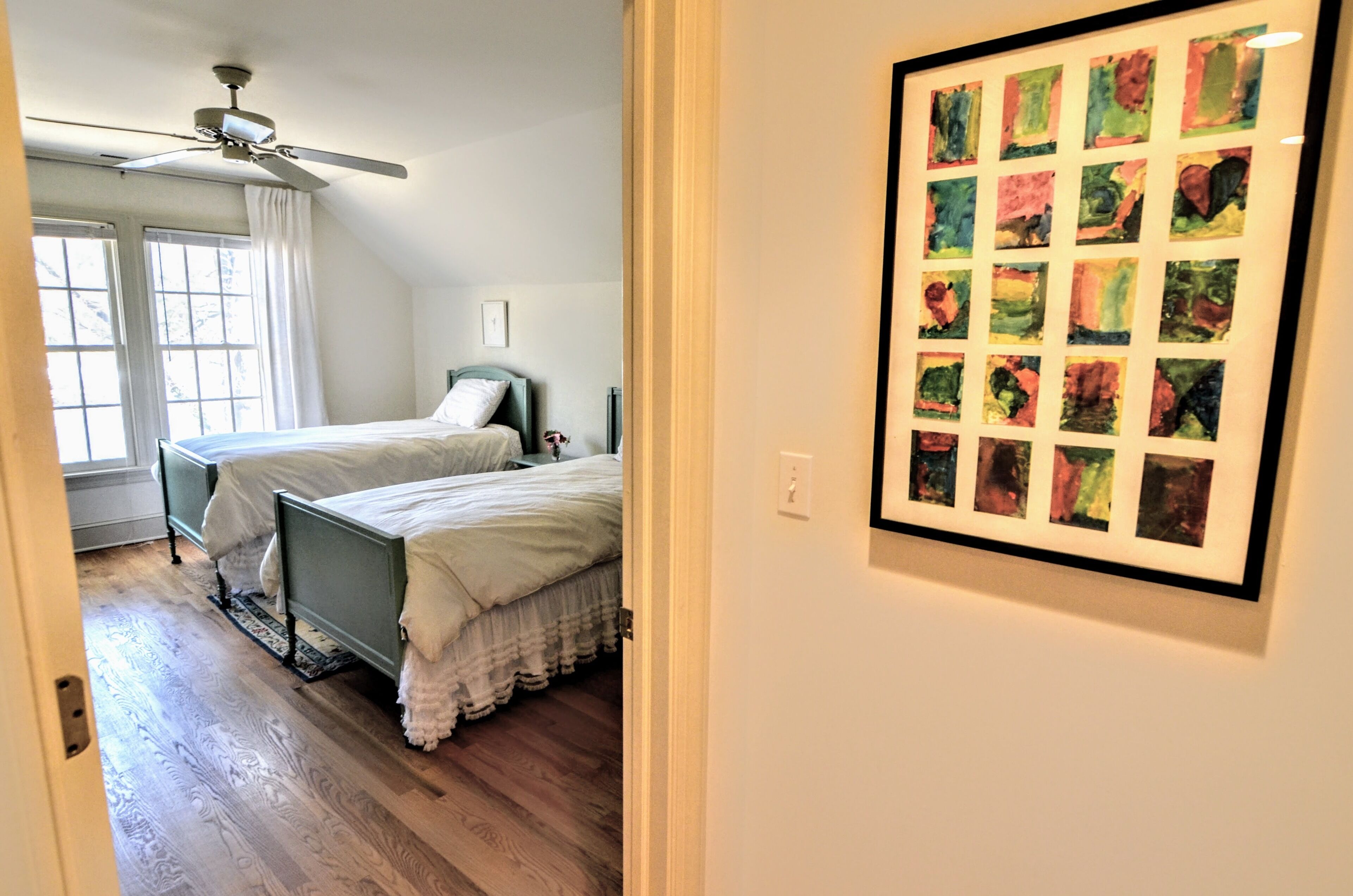 A bedroom with two beds, a ceiling fan, and a framed art piece on the wall.