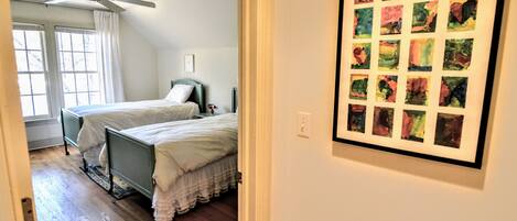 A bedroom with two beds, a ceiling fan, and a framed art piece on the wall.