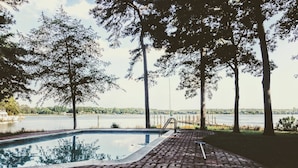Ein Swimmingpool mit einem Ziegelweg, umgeben von Bäumen und Blick auf einen See.