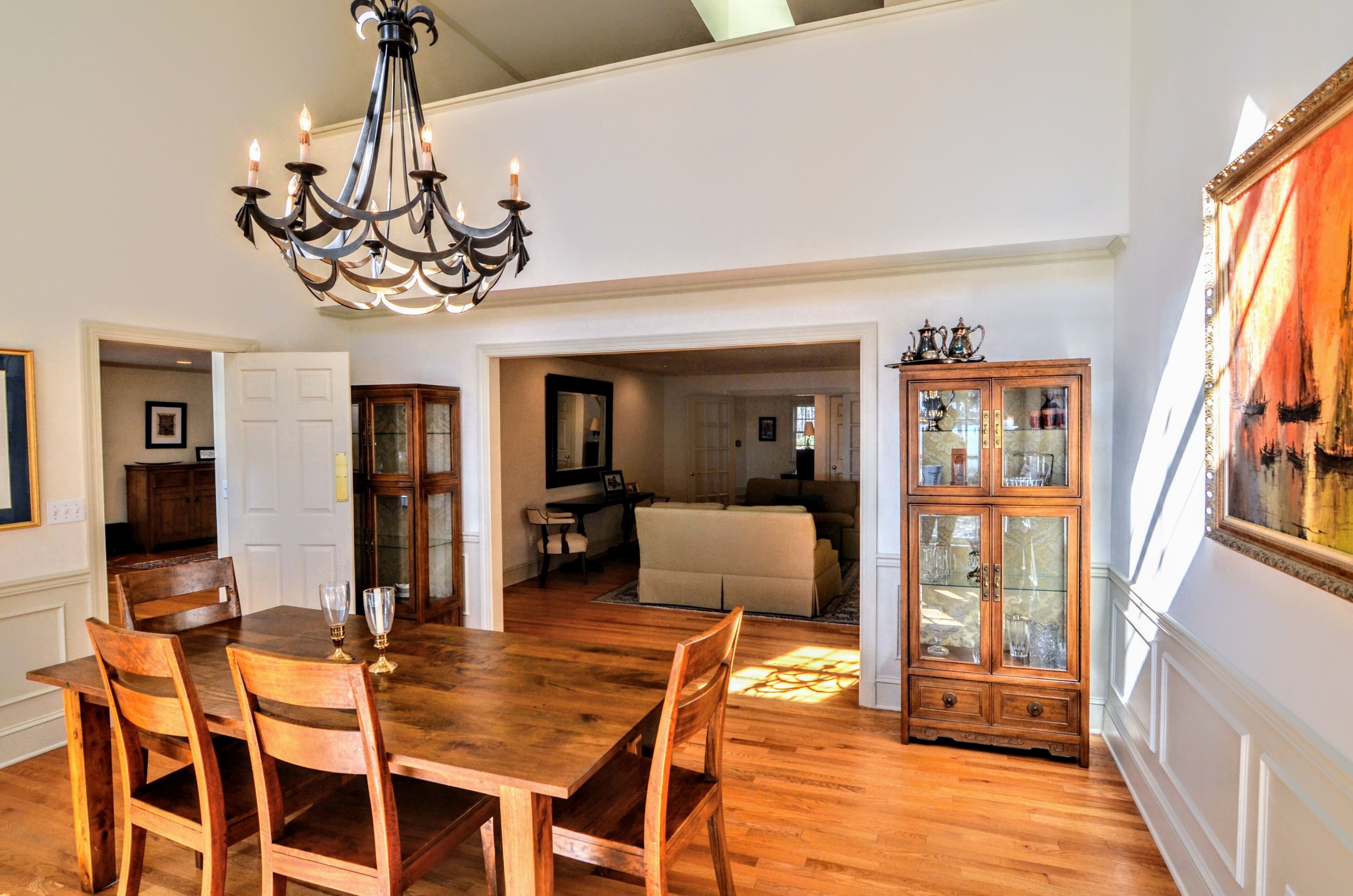 Un comedor con mesa y sillas de madera, una araña y un aparador con puertas de vidrio.