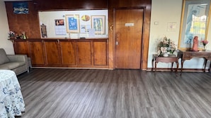 Zona de recepción con mostrador de madera, sofá, escritorio con una estatua y cuadros en la pared.