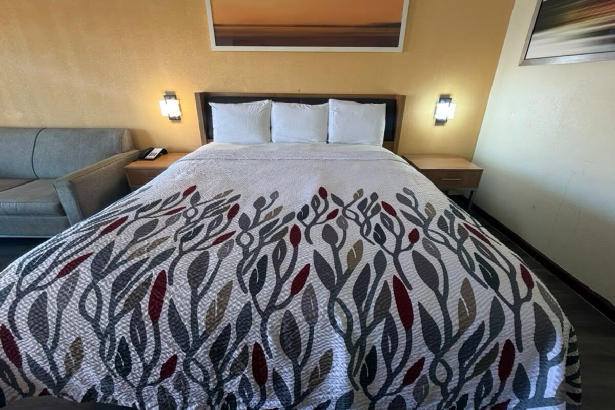 Una habitación de hotel con una cama, una mesita de noche, una lámpara, un sofá y un cuadro en la pared.