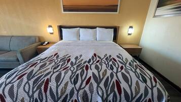 A hotel room with a bed, a nightstand, a lamp, a sofa, and a painting on the wall.