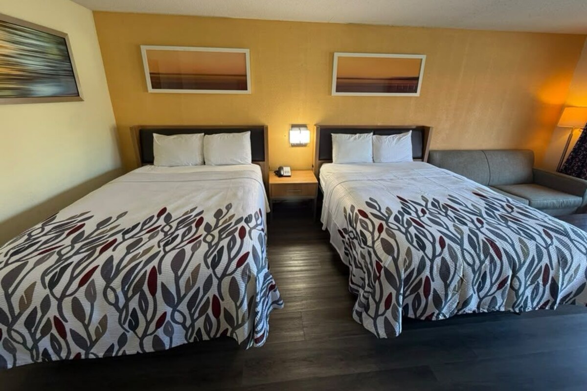 Habitación de hotel con dos camas, una mesita de noche, una lámpara y un sofá.