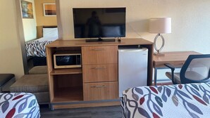 Habitación de hotel con cama, escritorio, televisión, microondas, refrigerador y una silla.