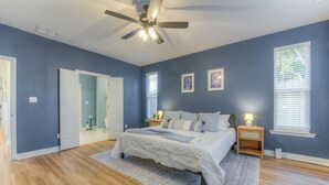 Une chambre à coucher comprenant un lit, un ventilateur de plafond, une table de chevet et une commode, ainsi qu’une fenêtre avec des stores.