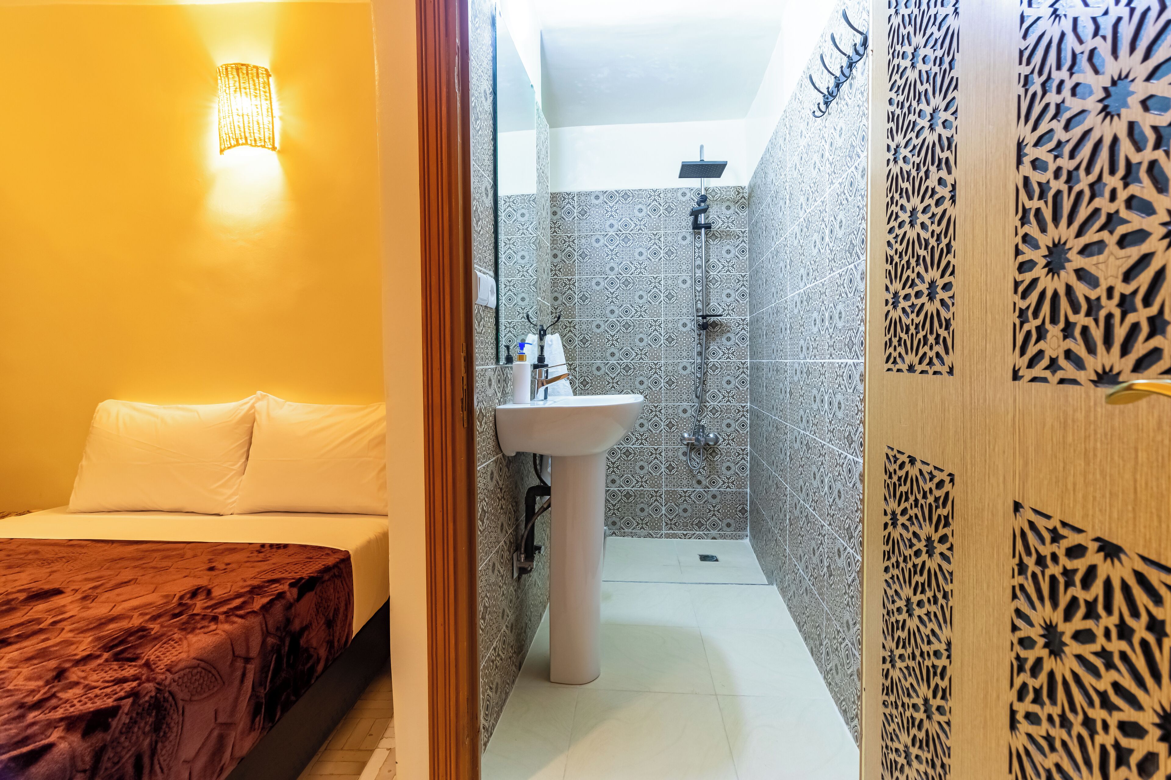 Een hotelkamer met een bed, een badkamer met wastafel en douche, en decoratieve wandpanelen.