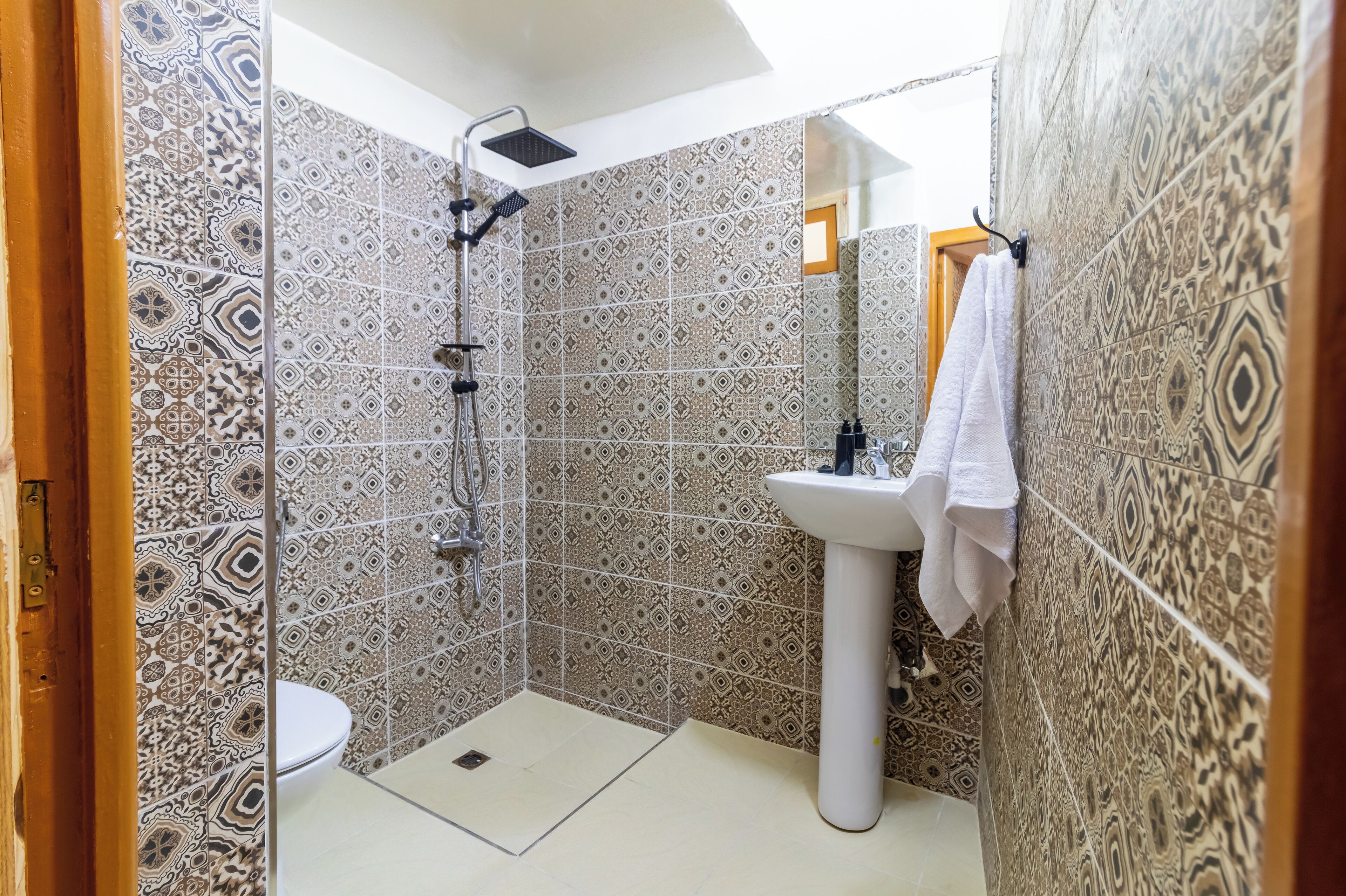 Une salle de bain avec des carreaux décorés, une douche, un lavabo et une serviette accrochée au mur.