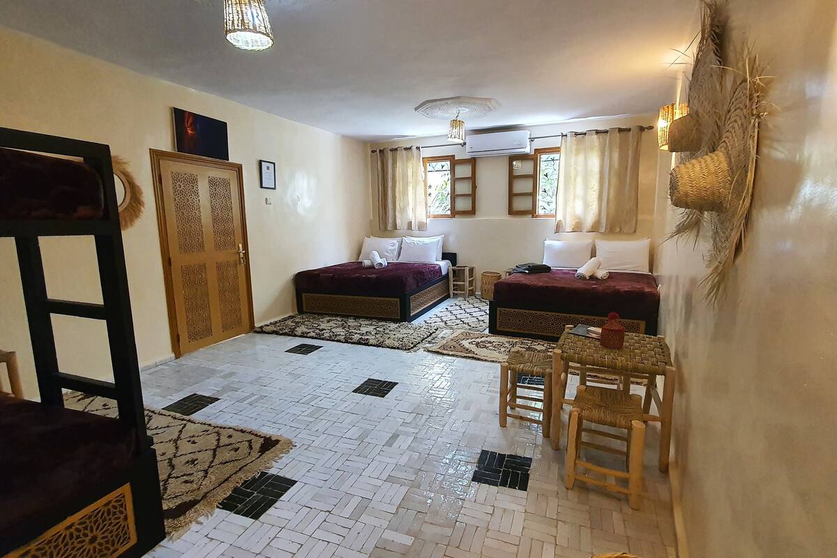 Une chambre avec deux lits, une petite table, une chaise, une décoration murale et un ventilateur de plafond.