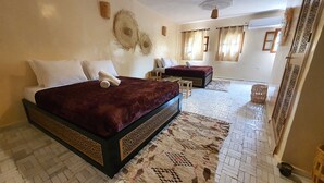 Una habitación de hotel con una cama grande, una cama más pequeña, una zona de estar y una alfombra estampada.