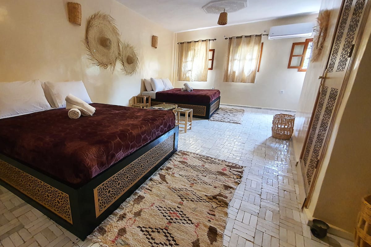 Une chambre d’hôtel avec un grand lit, un lit plus petit, un coin salon et une moquette à motifs.
