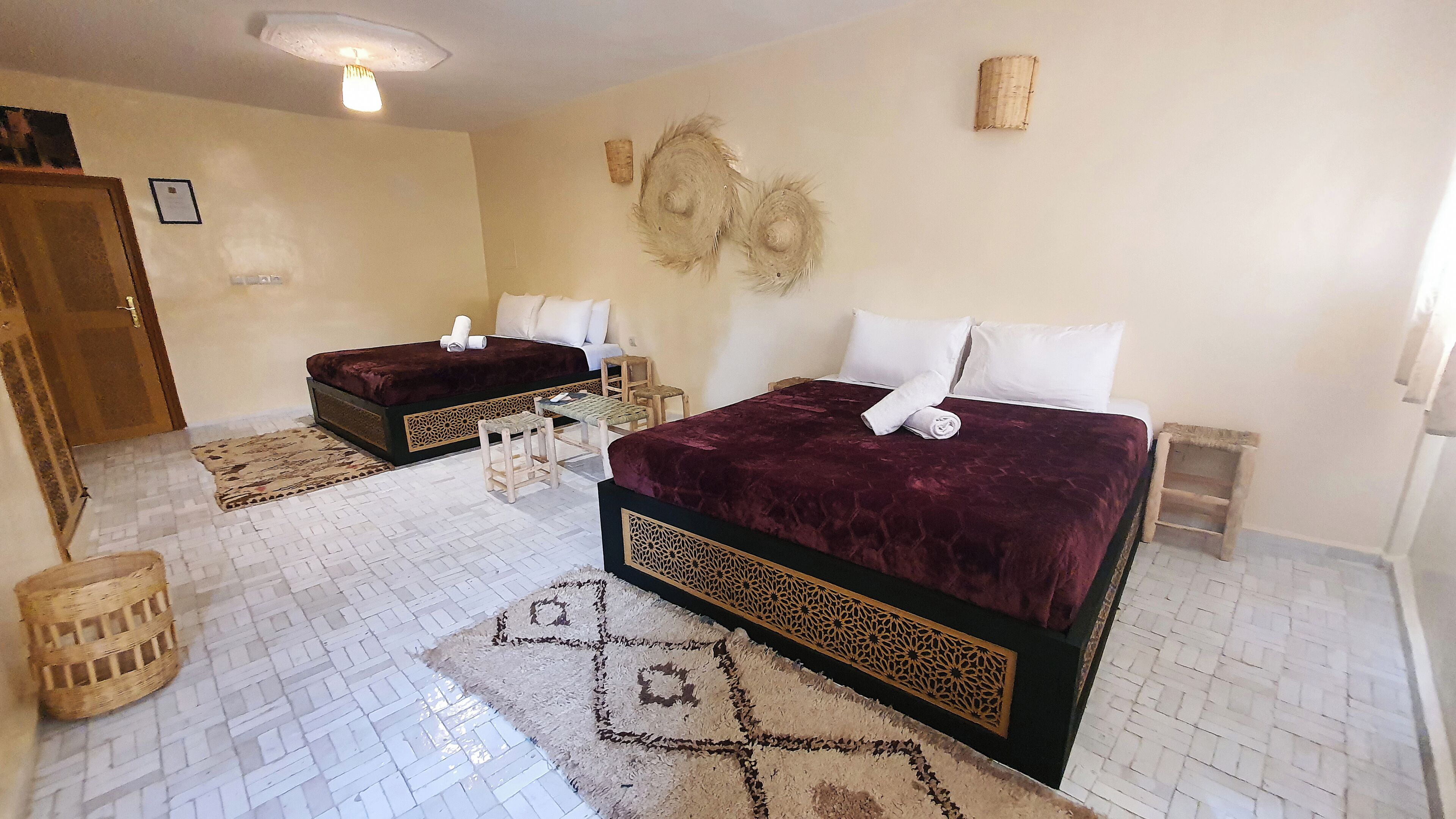 A hotel room with two beds, a small table, chairs, a patterned rug, and a decorative wall piece.