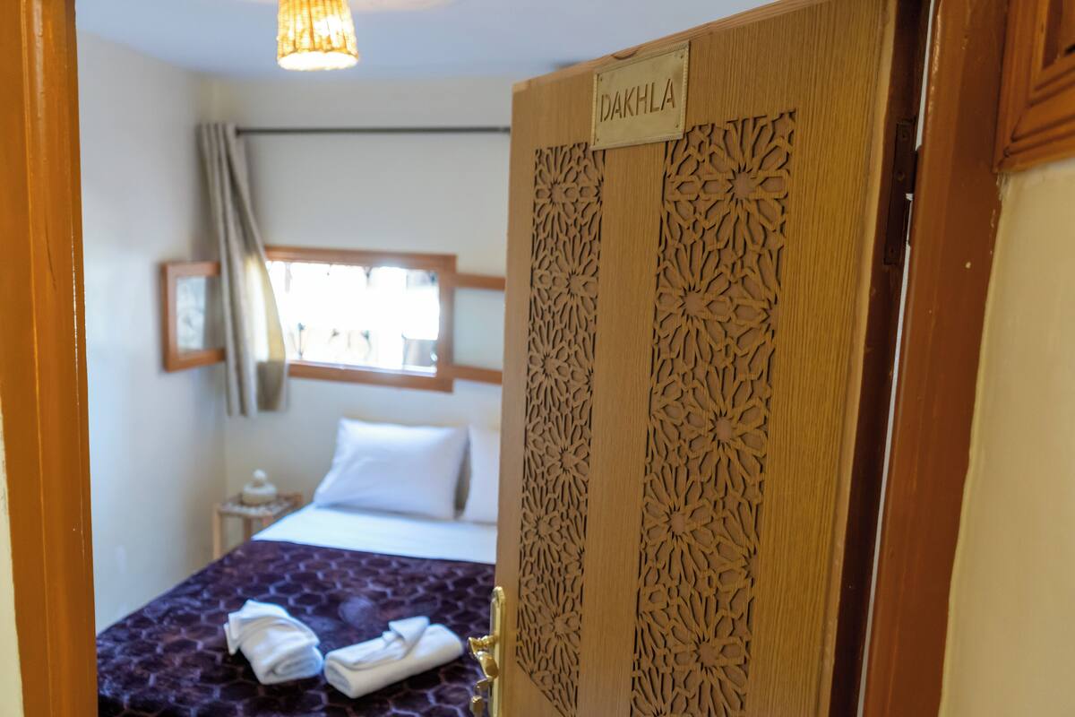 Une chambre d’hôtel avec un lit, une fenêtre avec des rideaux et une porte avec une plaque nominative.