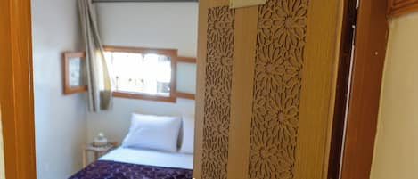 A hotel room with a bed, a window with curtains, and a door with a nameplate.