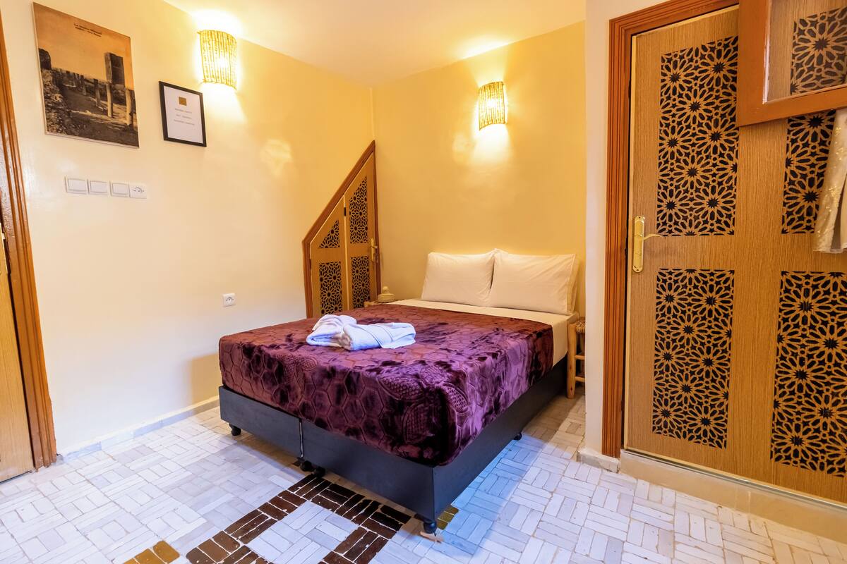 Une pièce avec un lit, une porte en bois ornée de motifs complexes et un luminaire fixé au mur.