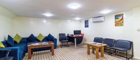 Ein Zimmer mit einem blauen Sofa, einem Holztisch, einem Schreibtisch mit Computer und mehreren Stühlen.
