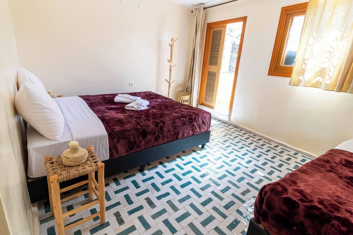 Une chambre à coucher avec un lit, un petit tabouret et un sol à motifs.