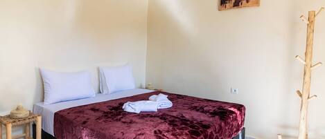 Una cama bien hecha con una colcha roja, almohadas blancas y una toalla doblada al lado.