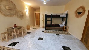 Una habitación con literas, un escritorio pequeño con una silla, una cesta tejida y una lámpara fijada a la pared.