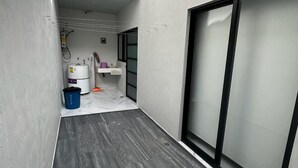 Un pasillo estrecho con piso de baldosas, pared blanca y un amplio vidrio corredero a la derecha.