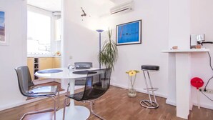 A modern kitchen with white cabinets, a white dining table, and black chairs. There is a blue abstract painting on the wall, a potted plant, and a vase with yellow flowers. - TERRACE DUPLEX at SAGRADA FAMILIA/GRACIA (Barcelona)