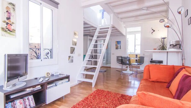 A living room with a TV, books, a red rug, and a staircase leading to an upper level. - TERRACE DUPLEX at SAGRADA FAMILIA/GRACIA (Barcelona)