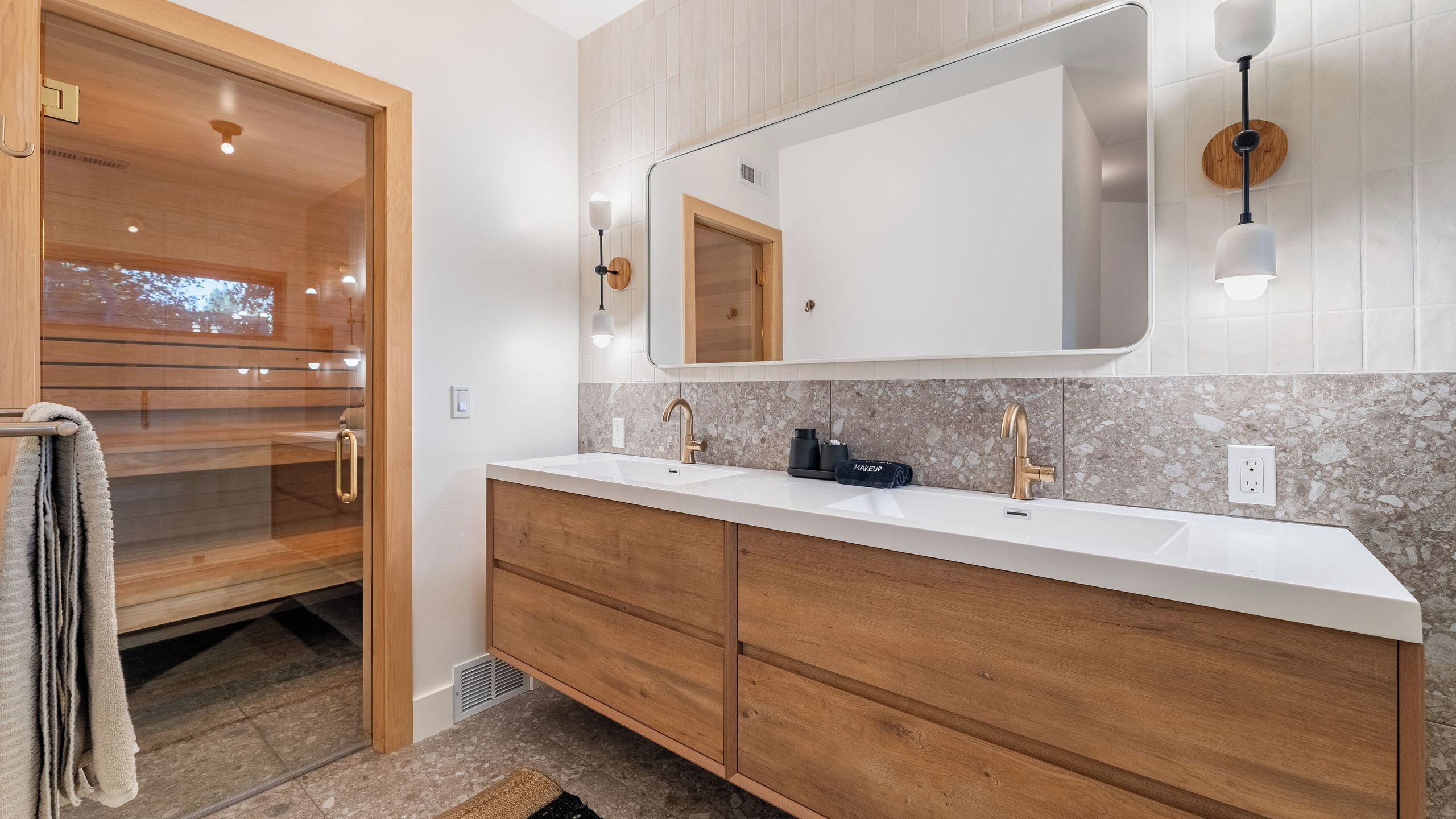 Un baño moderno con lavamanos doble, tocador de madera, un espejo grande y cabina de ducha con mampara de vidrio.