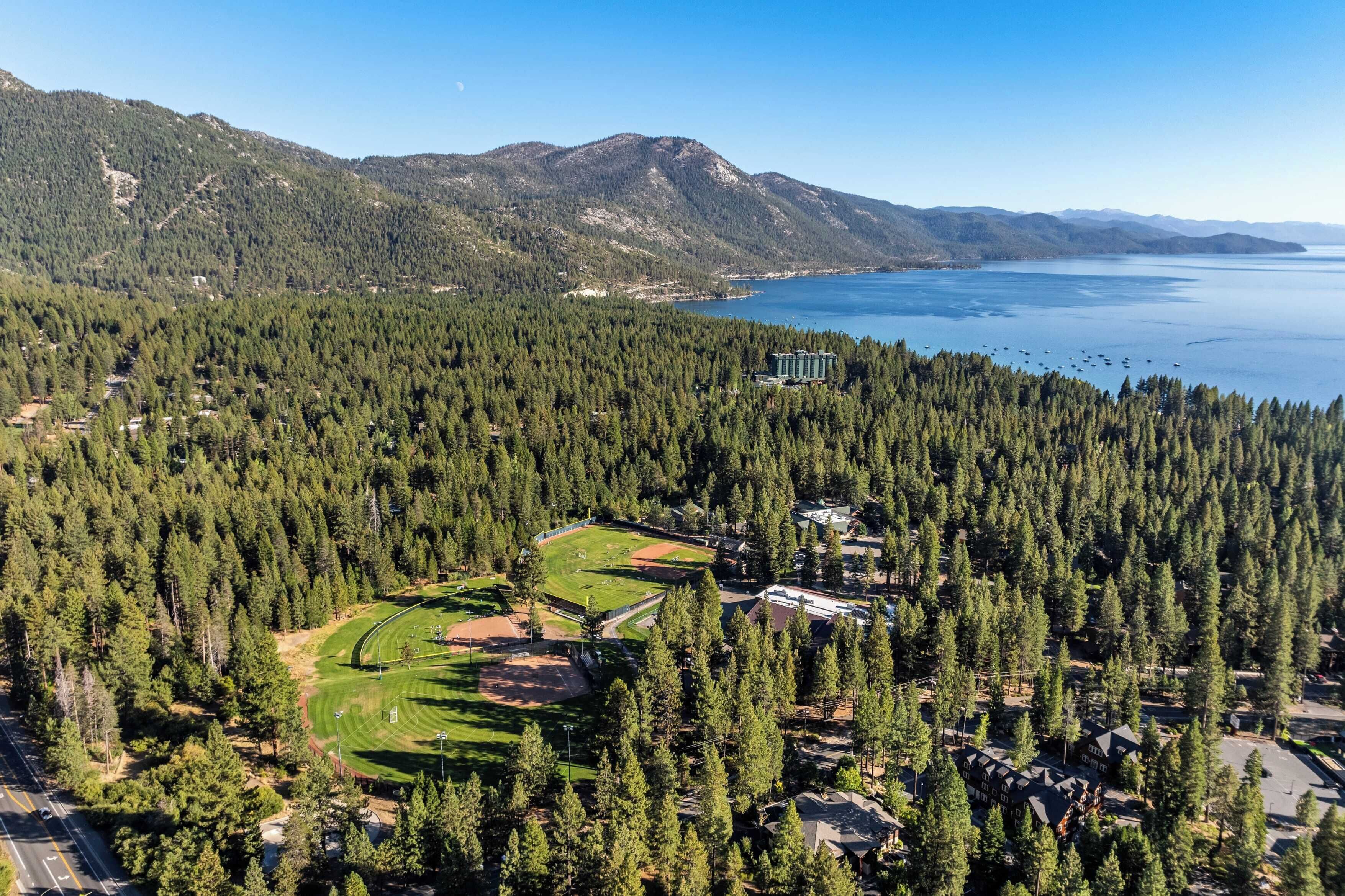 Un parcours de golf entouré d ’une forêt dense et de montagnes, avec un grand bâtiment au centre.