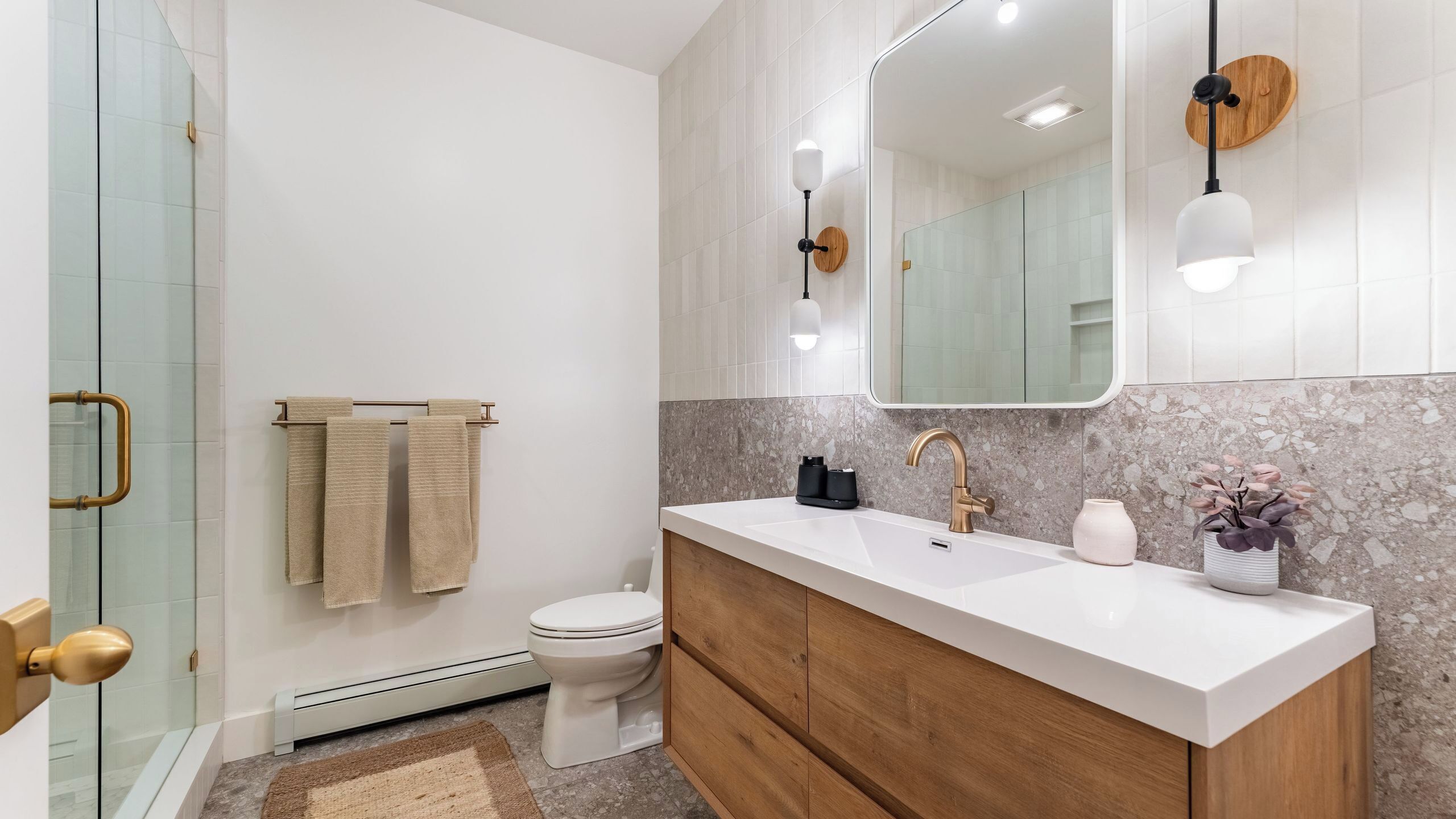 Een moderne badkamer met een douchecabine van glas, een toilet, een wastafelmeubel met een wastafel en een spiegel.