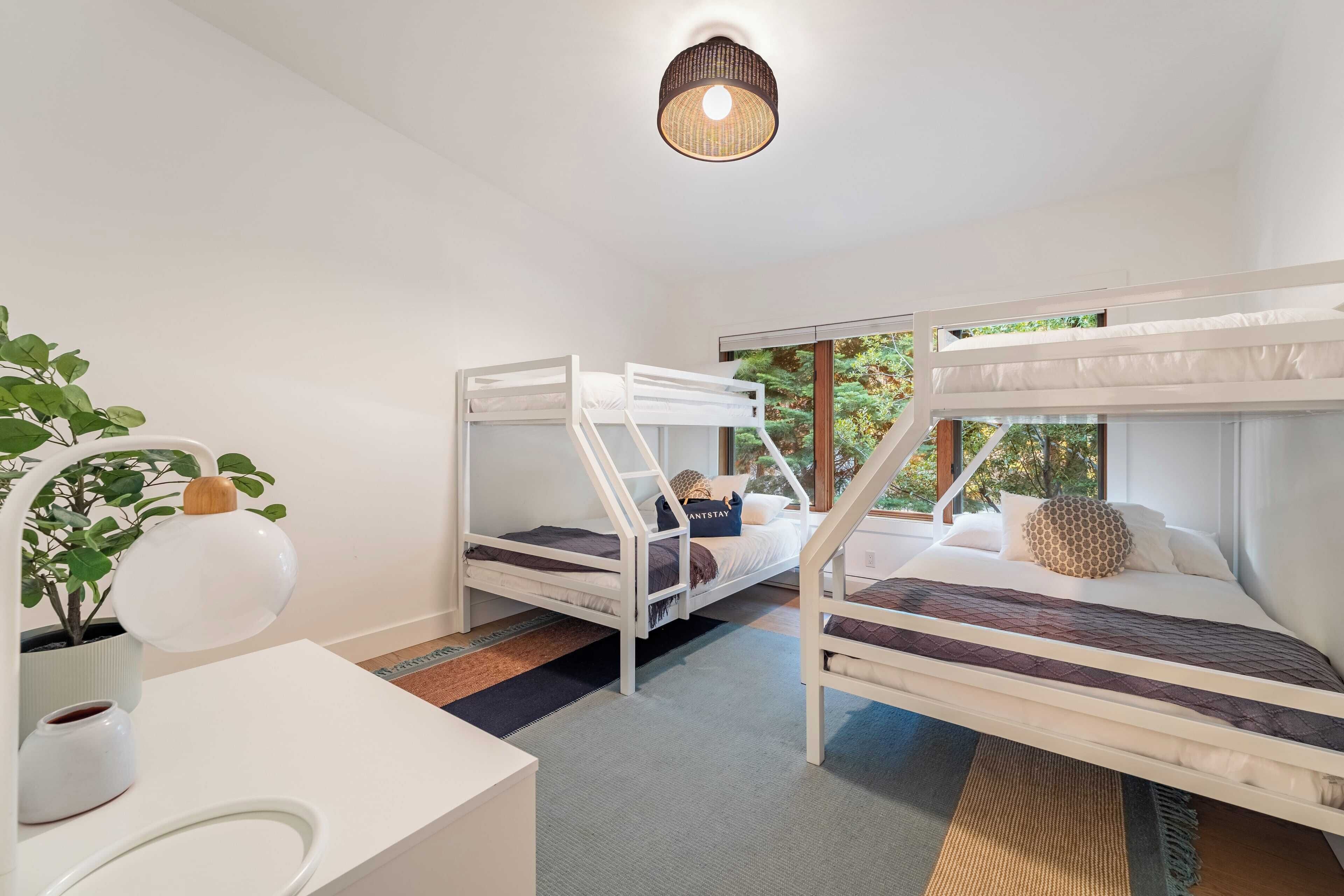 A room with bunk beds, a desk, a potted plant, and a hanging light fixture.