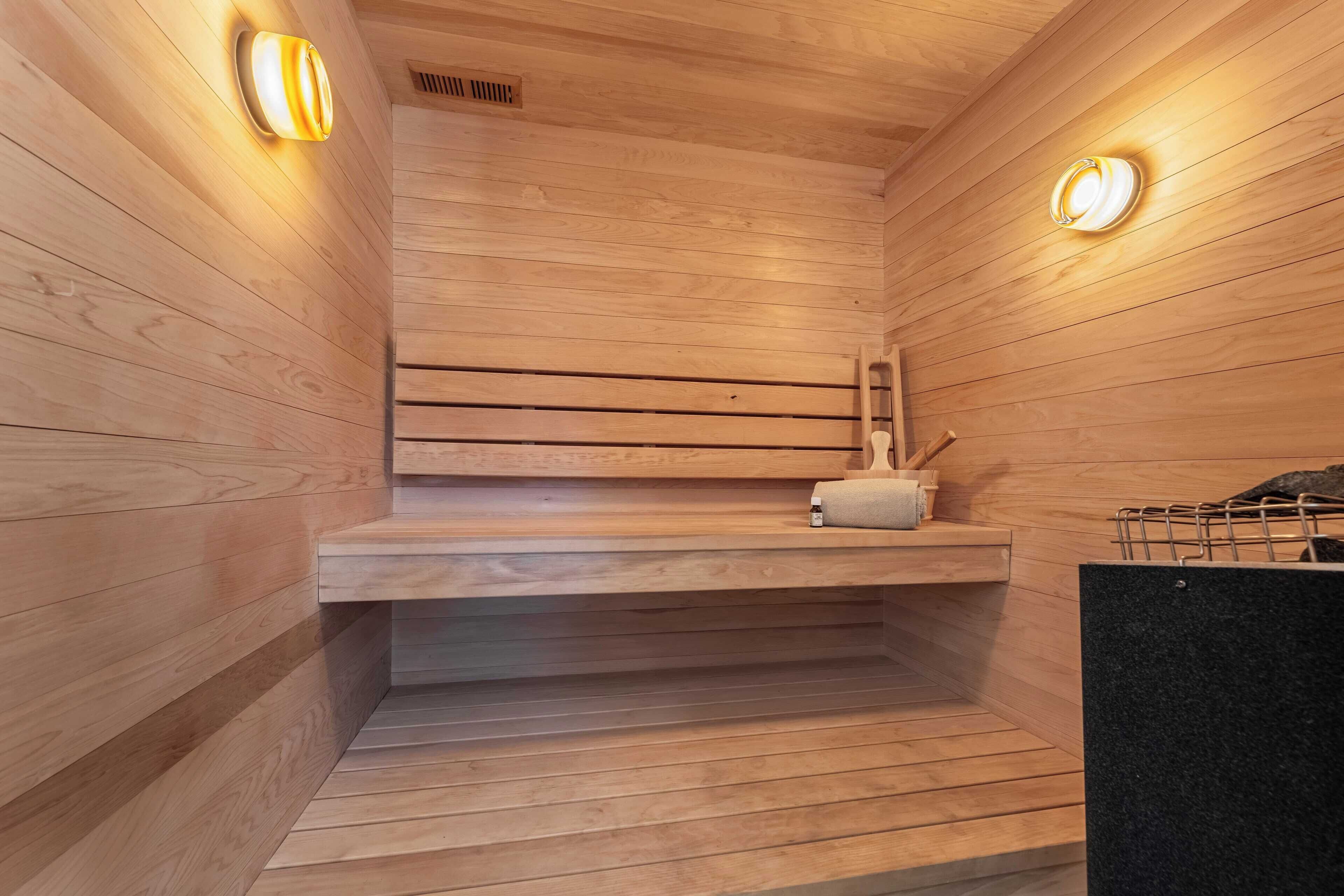 A wooden sauna with a bench, a towel, and a heater on a shelf.