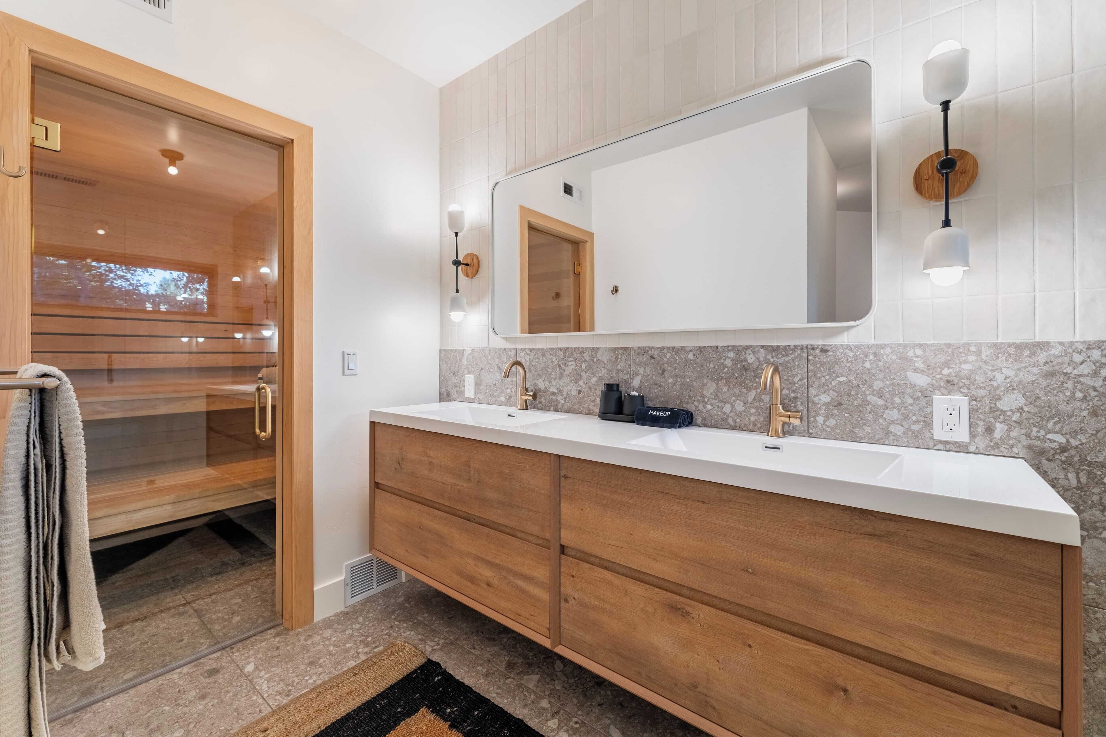 A modern bathroom with a wooden vanity, a large mirror, and a sauna door.
