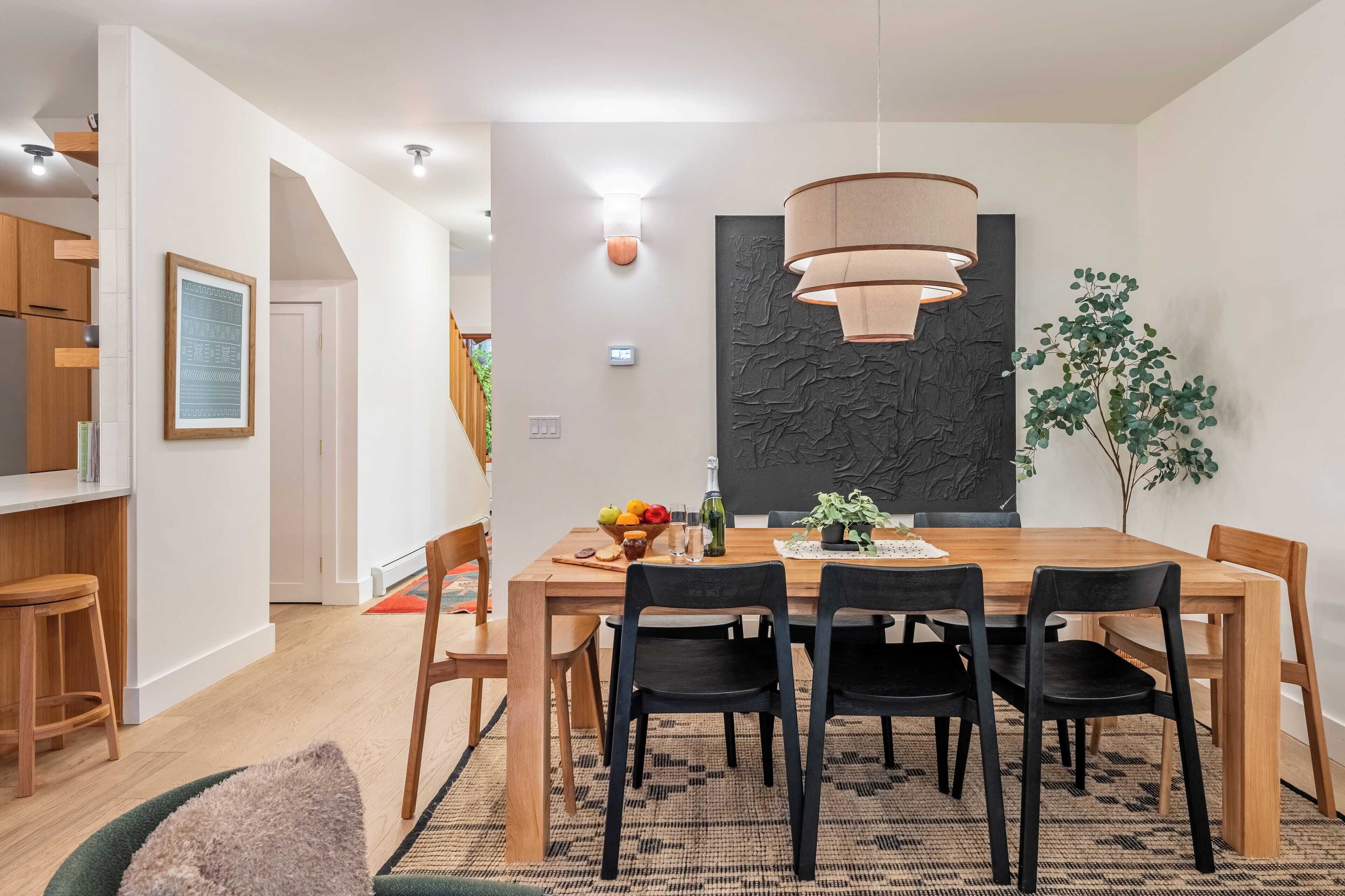 A modern dining area with a wooden table, black chairs, and a textured wall art piece.
