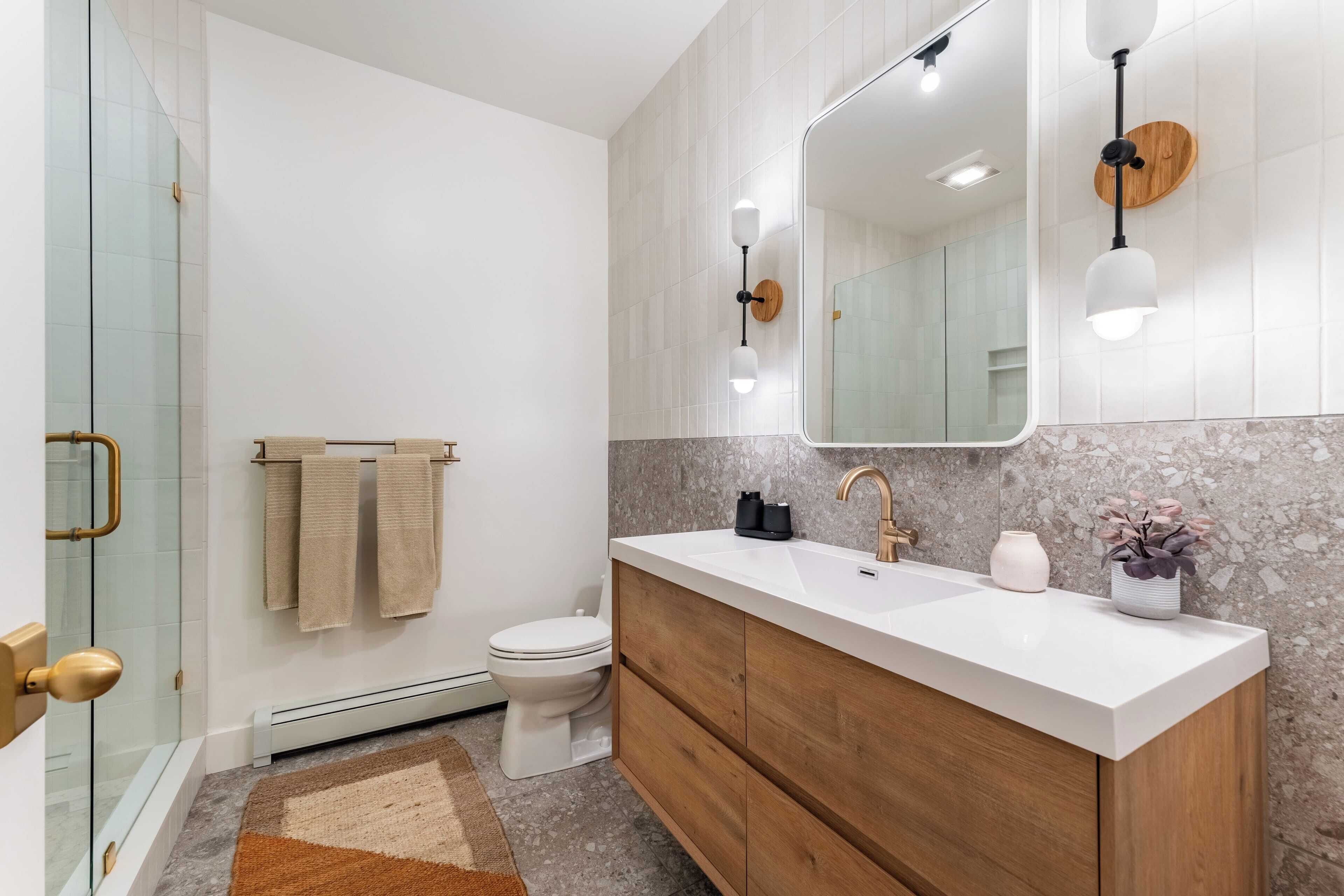 A modern bathroom with a glass shower enclosure, a white toilet, a wooden vanity with a white sink, and a marble backsplash.