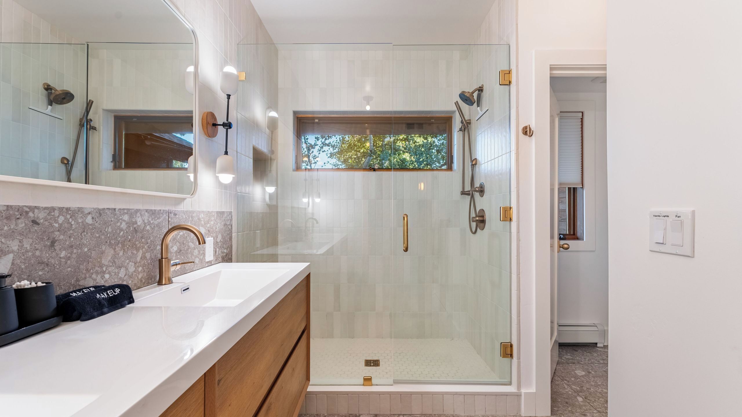 A modern bathroom with a glass-enclosed shower, a vanity with a marble countertop, and a large mirror.