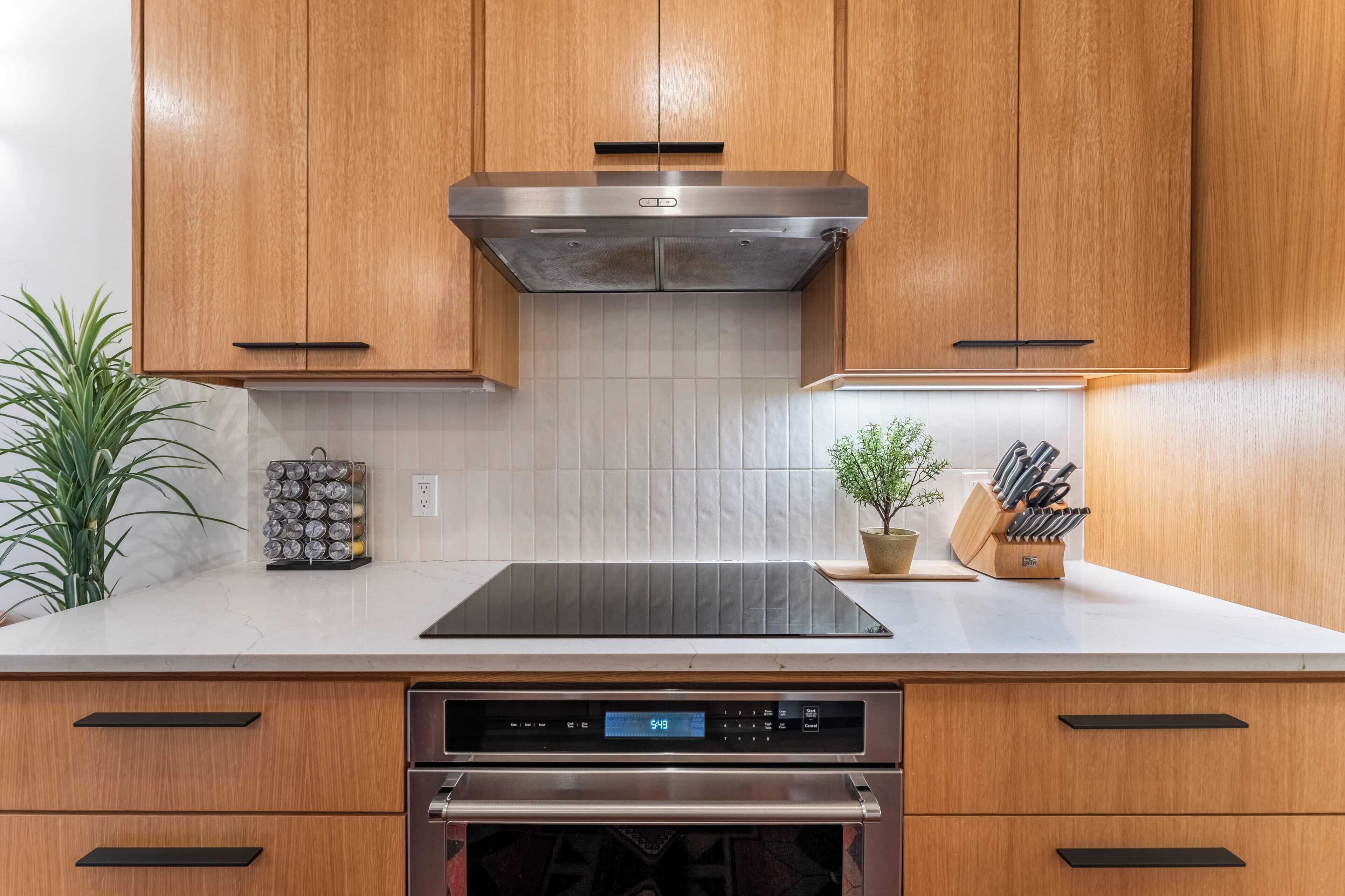 A kitchen with wooden cabinets, a stainless steel range hood, a built-in oven, and a countertop with a plant and a knife block.