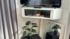 Un soggiorno con una TV a parete, un piccolo sgabello nero e due piante in vaso.